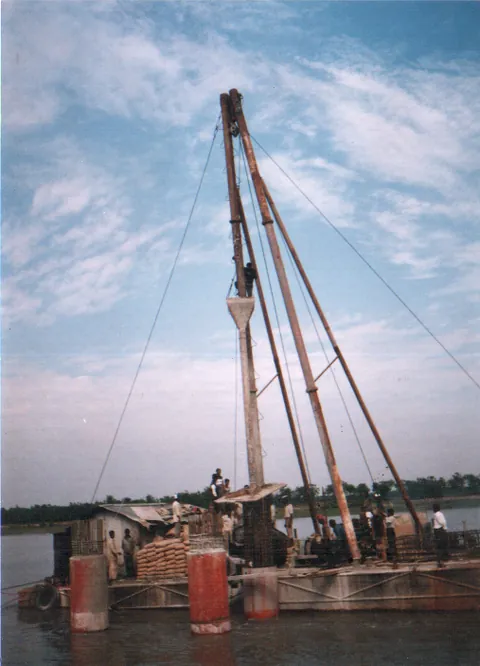 Pile driving derrick mounted on a barge in a river